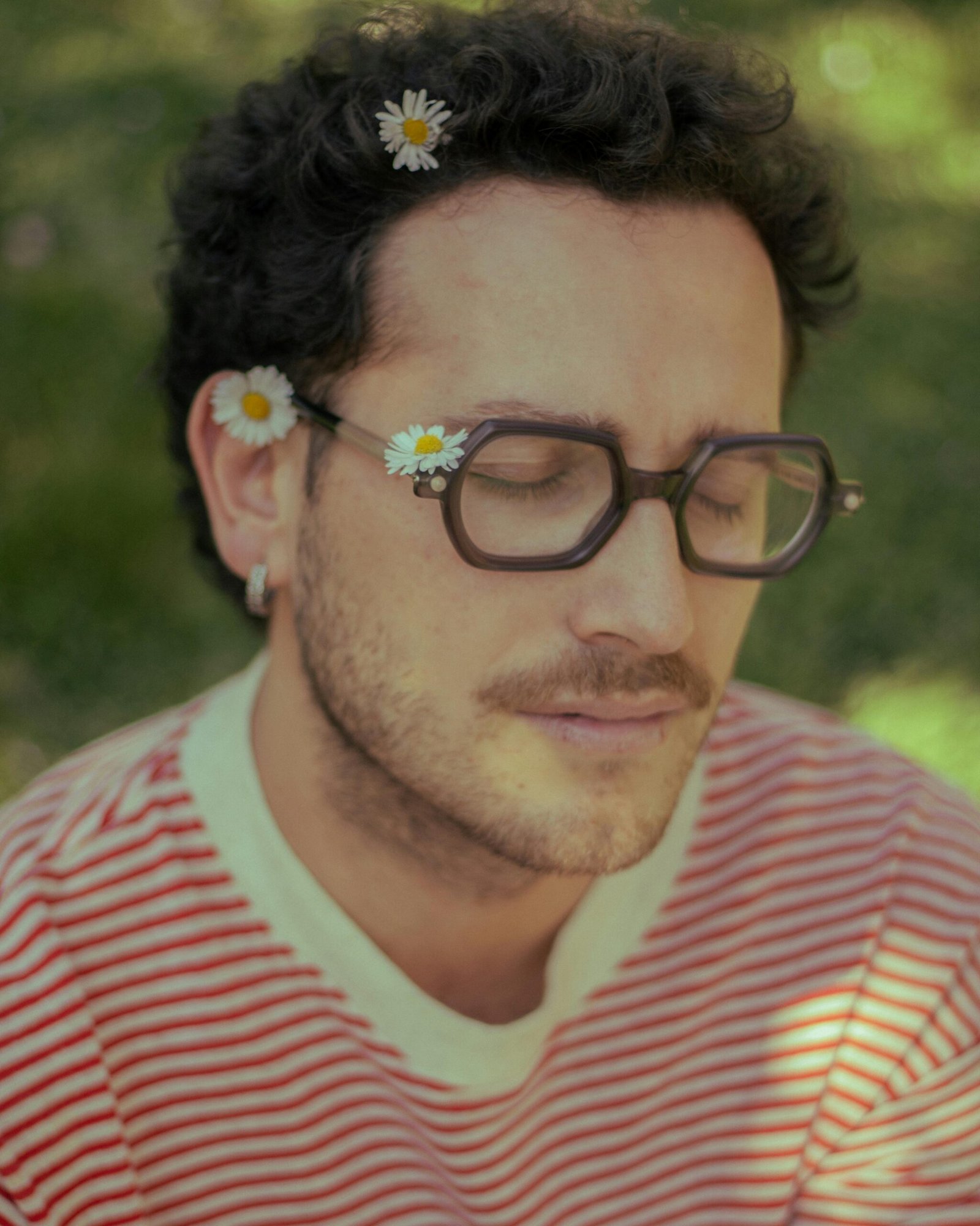 A relaxed man enjoying nature with daisies in his hair, creating a peaceful vibe in a sunny outdoor setting.